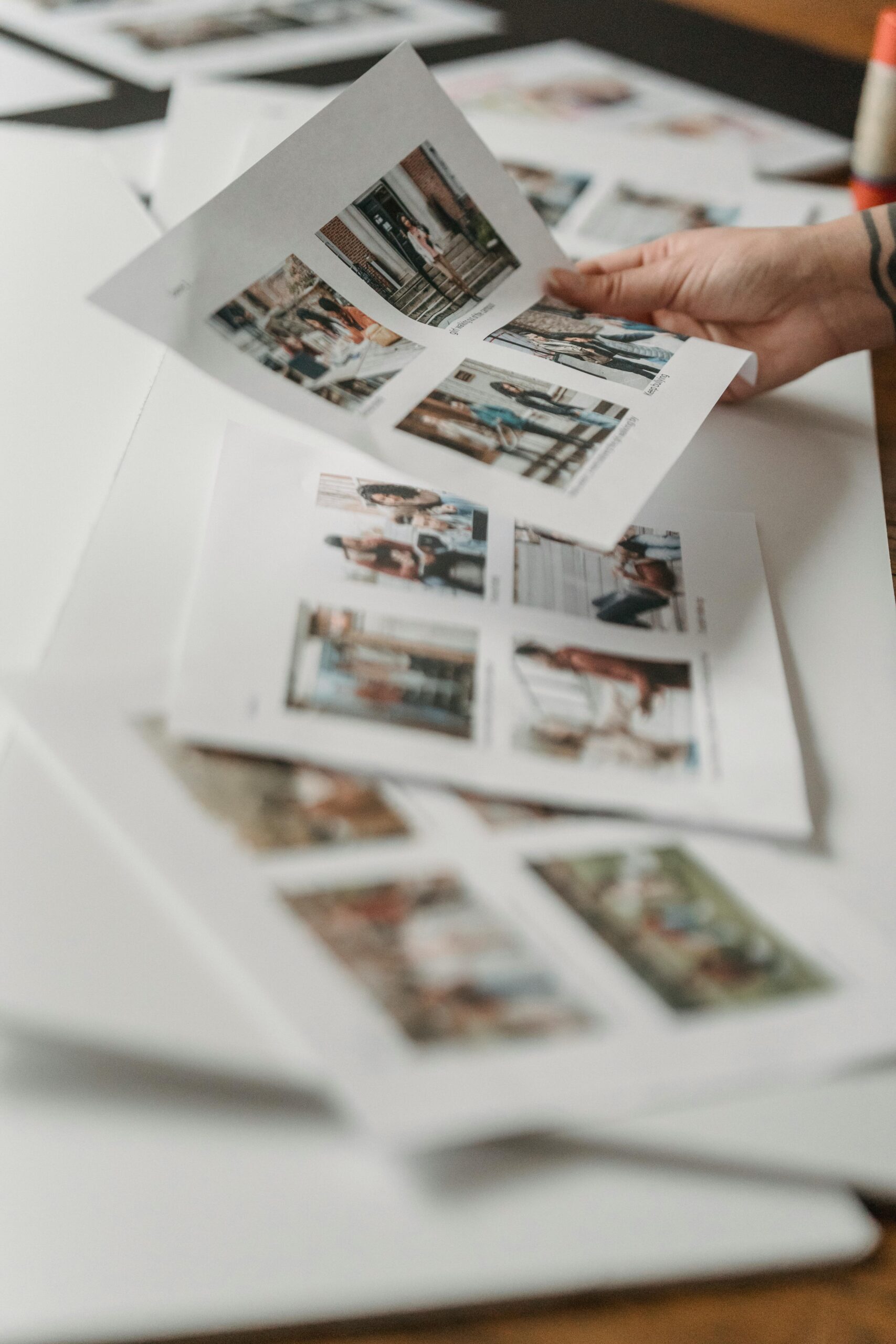 Crop anonymous person looking through printed photos scattered on floor in light room