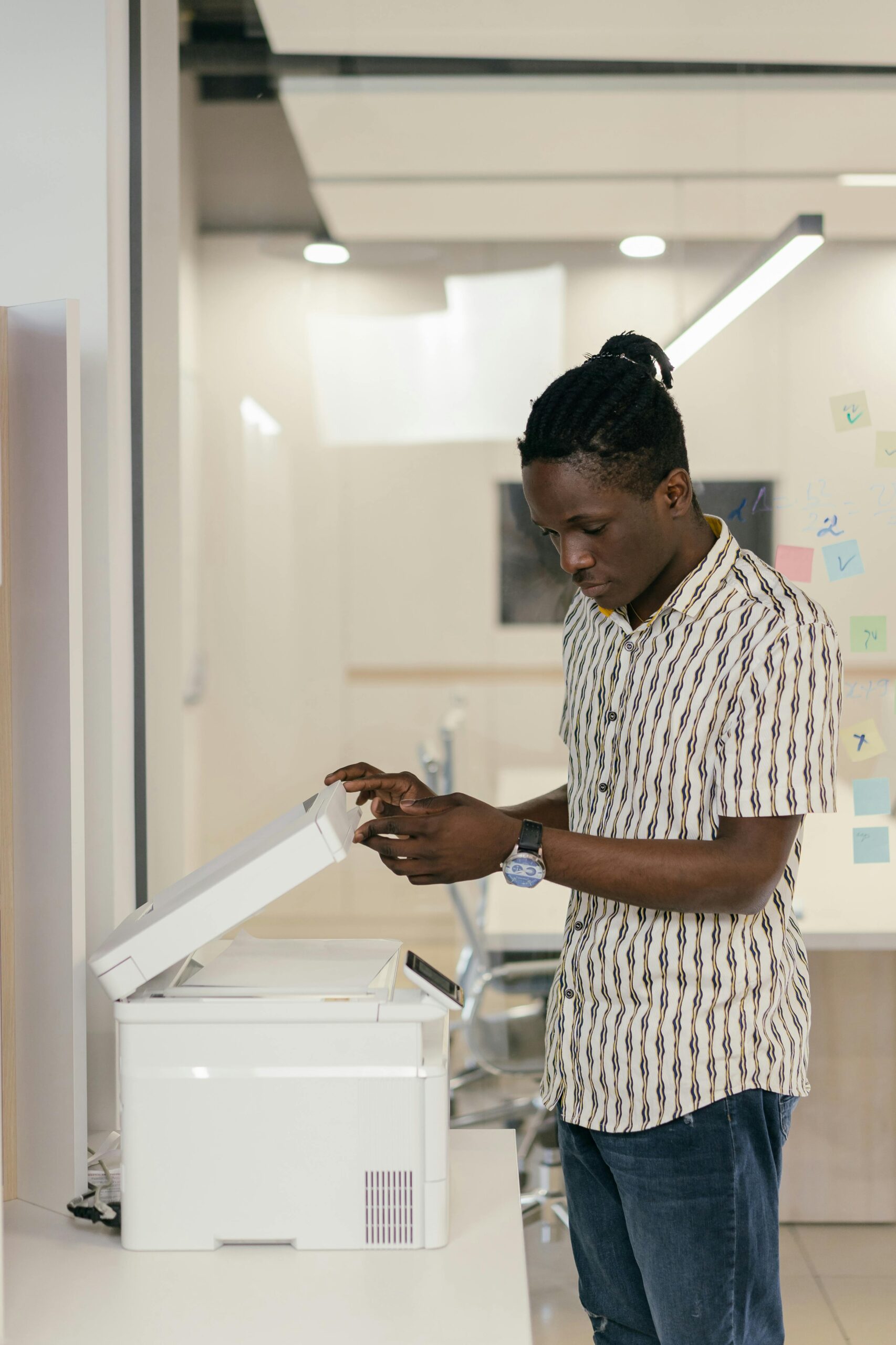 A young black man operates a photocopier in a modern office setting.